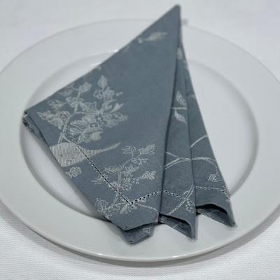 Guardanapo cinza com padrão floral sobre prato branco.