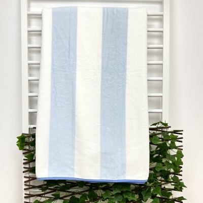 Toalha de banho azul e branca de riscas pendurada num suporte branco com ramos verdes