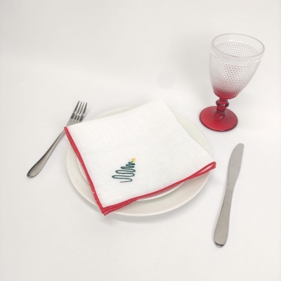 Conjunto de mesa com prato branco, guardanapo bordado, talheres e copo com base vermelha