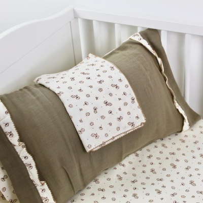 Almofada com padrão castanho e verde sobre almofada verde-cinza, lençol padrão castanho e verde, numa berço branco