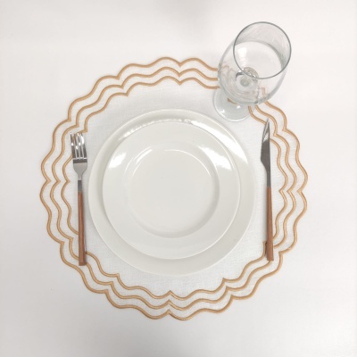 Conjunto de serviço de mesa com pratos brancos, talheres, copo de vidro e individual branco com bordas douradas.