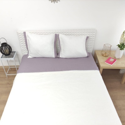 Cama de casal com roupa de cama branca e lilás, mesas de cabeceira com decorativos