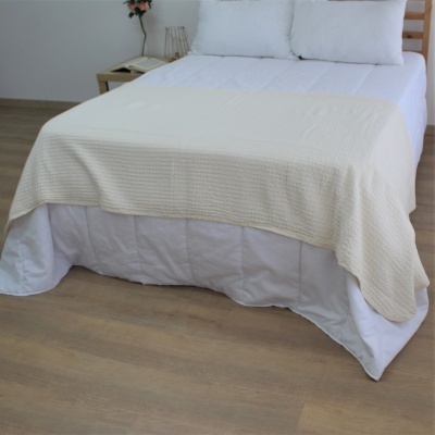 Cama de casal com roupa branca e manta bege em ambiente com piso de madeira clara