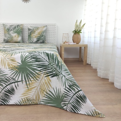 Jogo de cama com padrão de folhas verdes e bege em tecido branco, edredão e almofadas, mesa de madeira com vaso e cortinas brancas