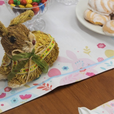 Coelho decorativo de palha e tecido sobre toalha com padrão floral ao lado de doces