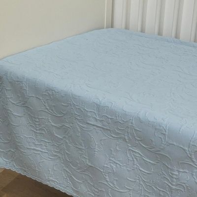 Colcha azul clara com padrão texturizado em relevo sobre cama