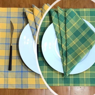 Conjunto de dois jogos americanos e guardanapos xadrez, amarelo e verde, com talheres e pratos brancos sobre mesa de madeira.