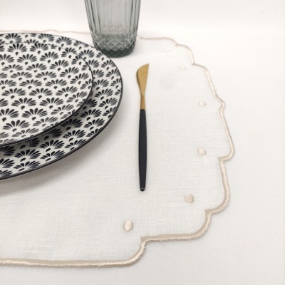 Conjunto de pratos, garfo, copo e individual branco com bordas decorativas.