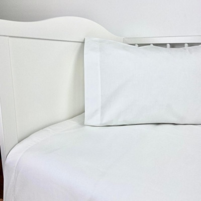 Roupa de cama branca numa cama de madeira branca com almofada e lençol.