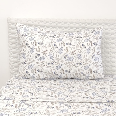 Jogo de cama com padrão floral azul e bege sobre cabeça de cama acolchoada branca