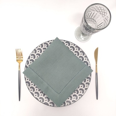 Conjunto de jantar com prato padrão preto e branco, guardanapo cinza-azulado, talheres preto e dourado, copo de vidro transparente.