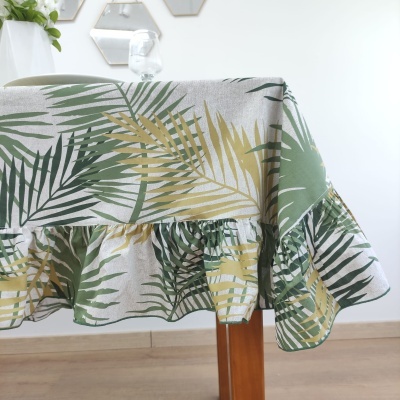 Toalha de mesa com padrão de folhas verdes e amarelas e babado numa sala com chão de madeira e paredes brancas