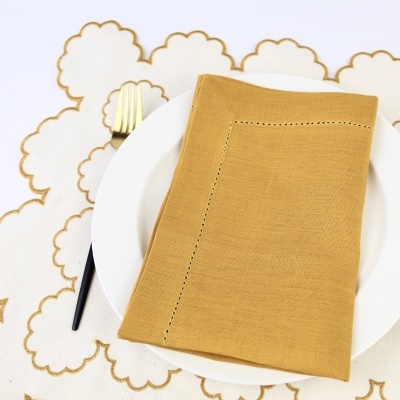 Guardanapo amarelo sobre prato branco com garfo dourado e toalhete branco com bordados dourados