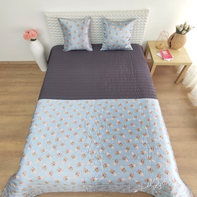 Cama com colcha azul clara floral e parte superior cinzento escuro com almofadas combinando