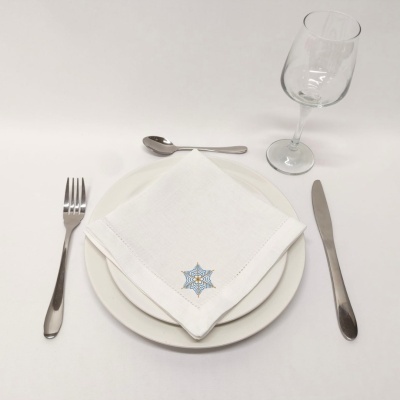 Conjunto de serviço de mesa com pratos brancos, guardanapo bordado, talheres de metal e copo de vidro