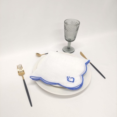 Conjunto de mesa com prato branco, guardanapo branco com borda azul, talheres e copo cinzento