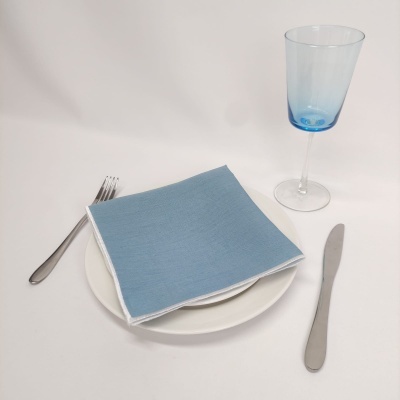 Mesa posta com prato branco, talheres de metal, guardanapo azul e copo de vidro azul