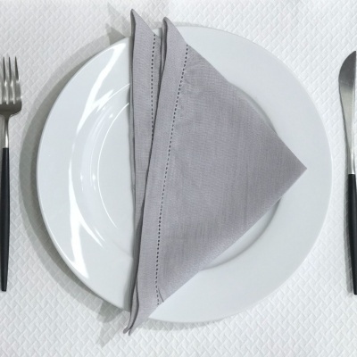 Conjunto de talheres com pratos brancos e guardanapo cinza sobre uma toalha branca.