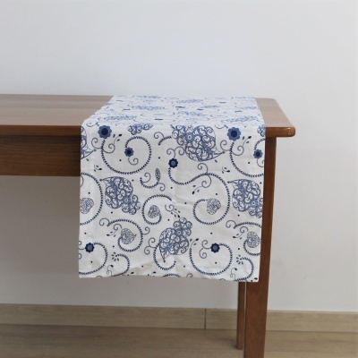 Caminho de mesa branco com padrão azul de arabescos e flores sobre mesa de madeira