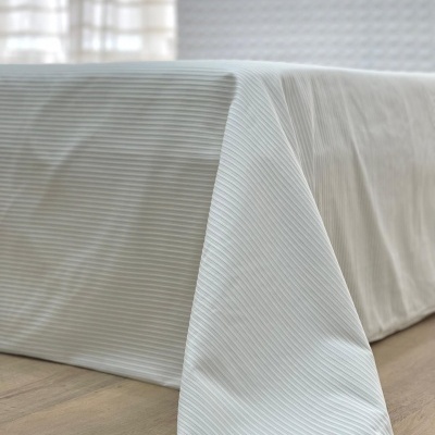 Toalha ou colcha branca com riscas finas sobre cama em quarto com paredes brancas texturizadas