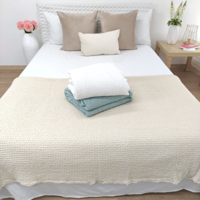 Cama arrumada com almofadas castanhas, manta bege e edredons branco e verde-azulado