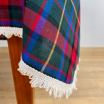 Tecido xadrez colorido com franjas brancas pendurado numa peça de madeira.