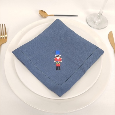 Guardanapo azul com bordado de soldado de brinquedo sobre prato branco, talheres dourados e copo de vidro