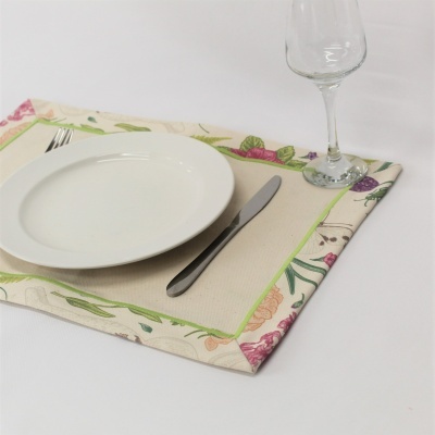 Mesa posta com prato branco, talheres, copo de vidro e individual de tecido com padrão floral