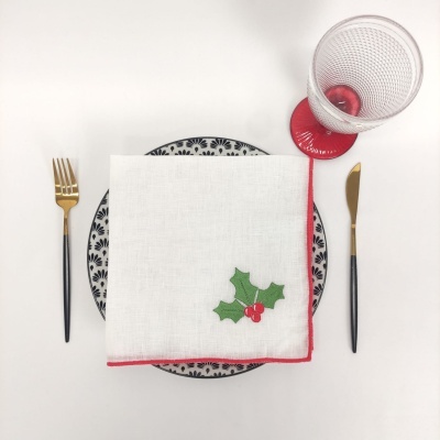 Conjunto de jantar com prato decorado, guardanapo com folha vermelha e verde, talheres dourados e copo com base vermelha.