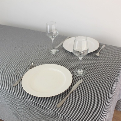 Mesa posta com toalha xadrez preta e branca, pratos brancos, copos de vidro e talheres