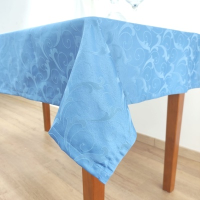 Toalha de mesa azul com padrão de arabescos em relevo pendurada num canto de mesa de madeira
