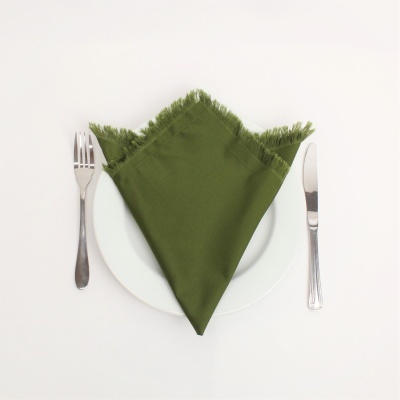 Guardanapo verde tecido com franjas num prato branco com talheres