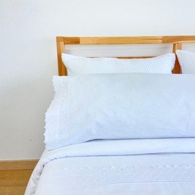 Conjunto de roupas de cama branco com bordados numa cama com cabeceira de madeira