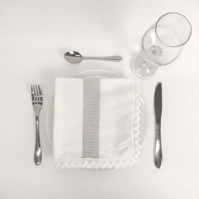 Talheres inox, prato branco, guardanapo branco com padrão cinza e renda, copo de vidro