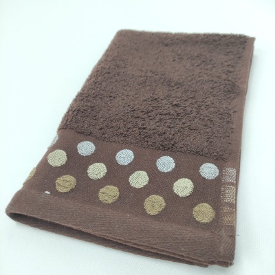 Toalha castanha com padrão de bolinhas na borda sobre fundo branco