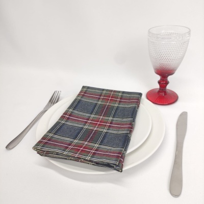 Conjunto de mesa com prato branco, guardanapo xadrez, talheres metálicos e copo de vidro com base vermelha