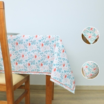 Toalha de mesa branca com padrão floral azul, verde e laranja sobre mesa de madeira