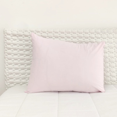 Almofada rosa clara sobre cama branca com cabeceira trançada branca