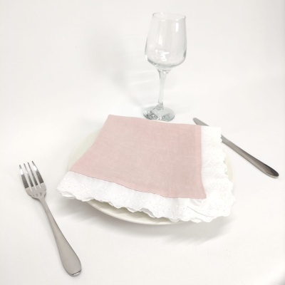 Guardanapo rosa com bordado branco sobre prato branco com talheres e copo de vidro