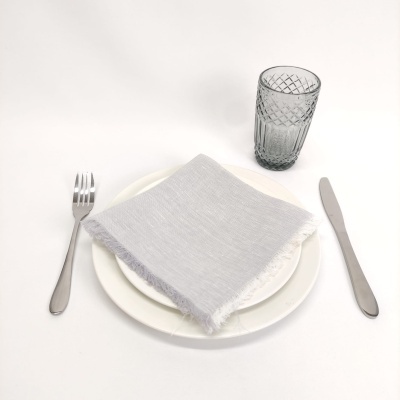 Conjunto de jantar com prato branco, guardanapo cinzento claro, talheres prateados e copo de vidro cinzento