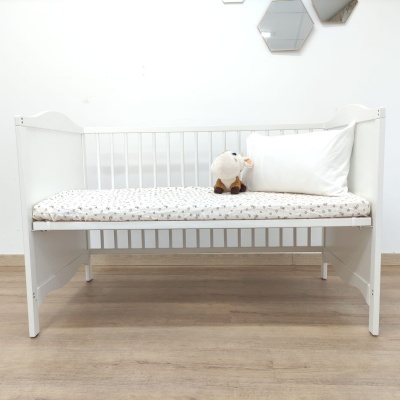 Berço branco com colchão estampado, almofada e peluche numa divisão minimalista