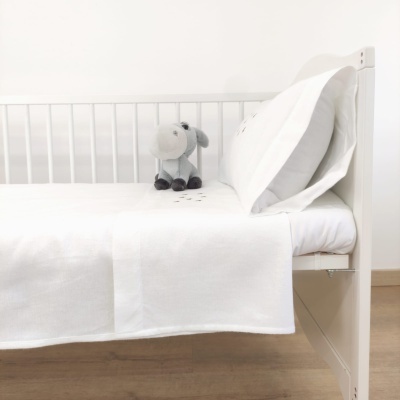 Cama branca com roupa de cama branca e peluche cinzento em forma de ovelha.
