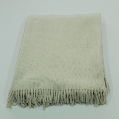 Manta creme com franjas numa superfície branca