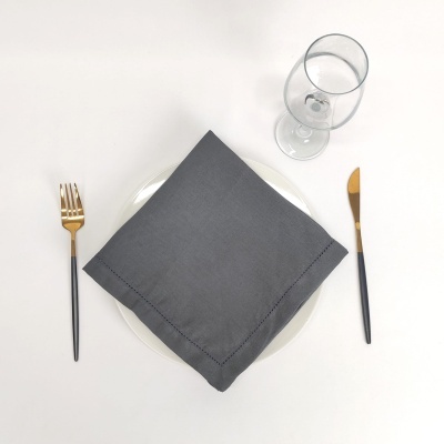 Conjunto de talheres com garfo dourado, faca dourada, guardanapo cinzento, prato branco e copo transparente