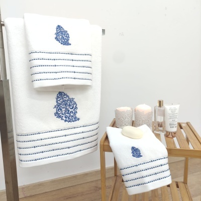 Toalhas brancas com bordado azul em ambiente de casa de banho