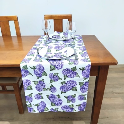 Caminho de mesa branco com padrão de flores roxas em mesa de madeira com pratos e copos