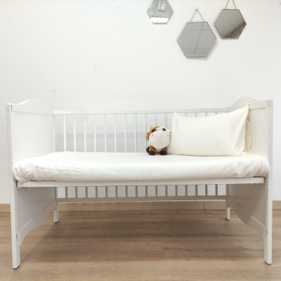 Cama de criança branca com almofada e peluche, três espelhos hexagonais na parede