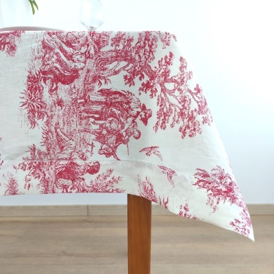 Toalha de mesa branca com padrão vermelho de cenas naturais sobre mesa de madeira.