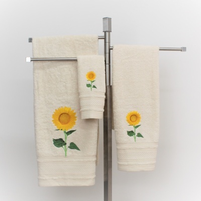 Três toalhas creme com bordado de girassol penduradas num suporte metálico.