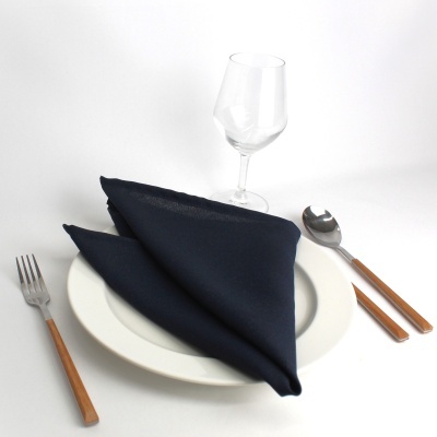 Conjunto de jantar com prato branco, guardanapo preto, talheres com cabos de madeira e copo de vidro